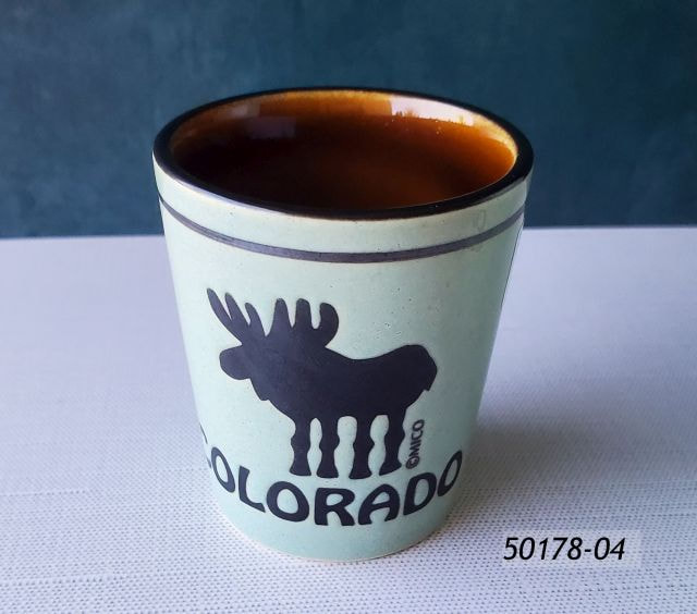 50178-04 Colorado Souvenir shot with aqua ceramic glaze and inner brown glaze.  Design is debossed in black with a comic moose Colorado design. 