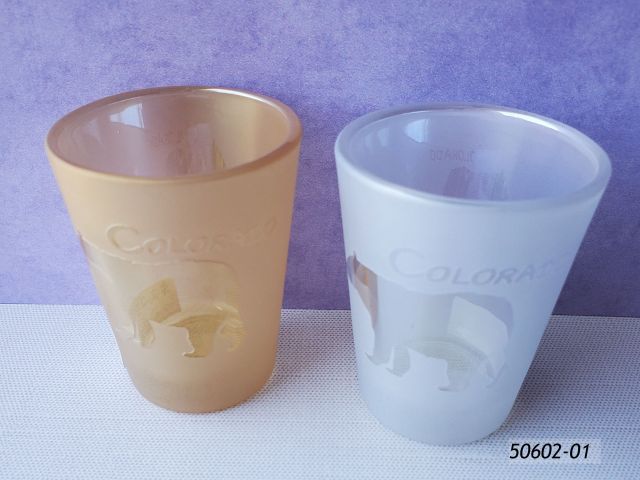 50602-01 Colorado Souvenir Shotglasses with pearlescent finish, two assorted colors, amber and silvery white. Design is a reverse image bear, clear and reflective against the matte "foggy" finish of the glass.  