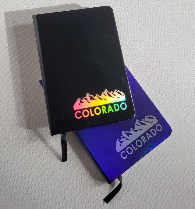 50745-01 Colorado Iridescent souvenir journal, 6" tall, lined pages.  2 assorted colors, blue and black. Iridescent Mountains design. 